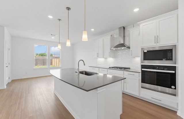 kitchen featuring stainless steel appliances, wall chimney range hood, a sink, light wood finished floors, and white cabinetry