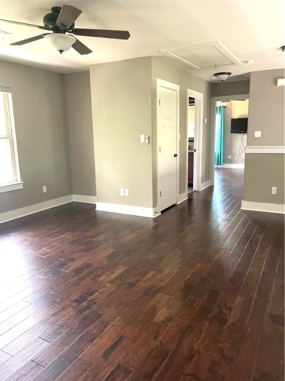 unfurnished room with dark wood finished floors, ceiling fan, baseboards, and attic access