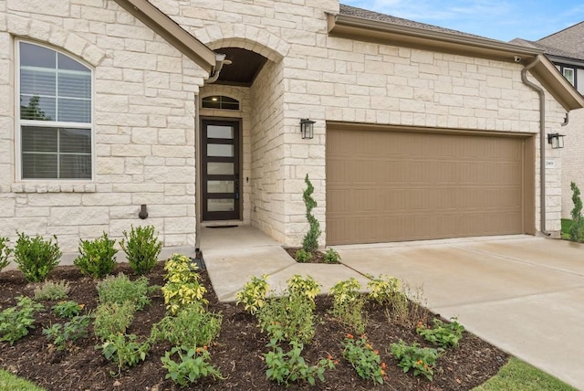 entrance to property with a garage, stone siding, and concrete driveway
