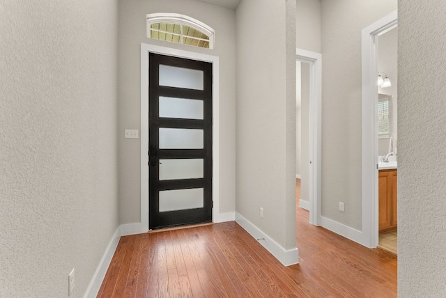 foyer with light wood finished floors, a textured wall, and baseboards