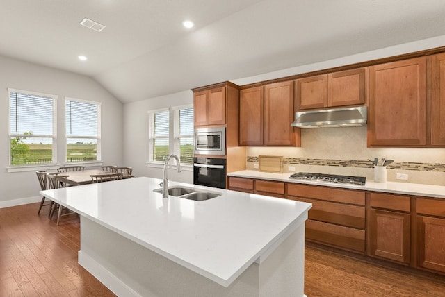 kitchen featuring under cabinet range hood, a sink, lofted ceiling, brown cabinets, and backsplash
