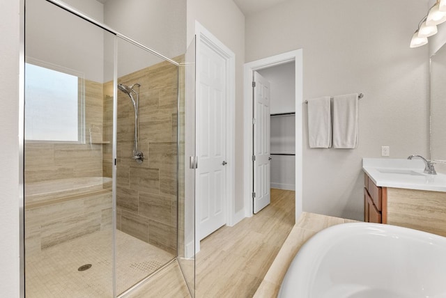 full bath with a stall shower, vanity, a bathtub, and wood finished floors