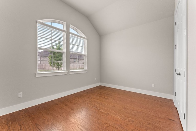 empty room featuring wood finished floors, lofted ceiling, and baseboards