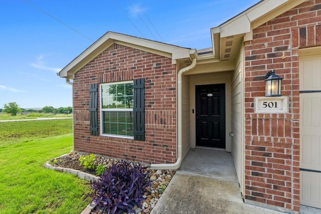 view of exterior entry with brick siding and a lawn