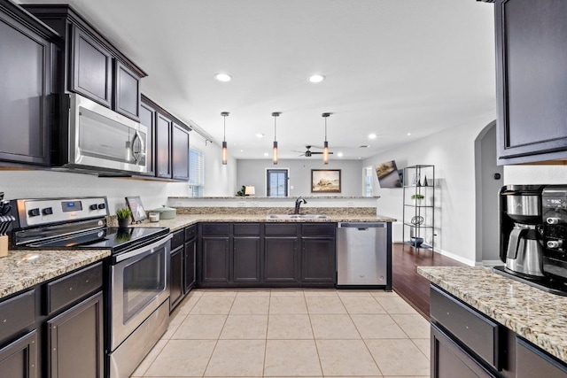 kitchen featuring appliances with stainless steel finishes, a peninsula, light stone counters, light tile patterned floors, and recessed lighting