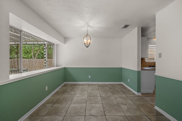 tiled spare room with a chandelier, a textured ceiling, and baseboards