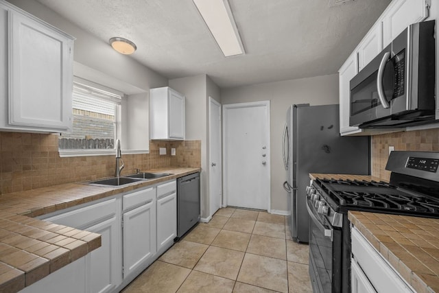 kitchen featuring stainless steel appliances, a sink, tile counters, white cabinets, and decorative backsplash
