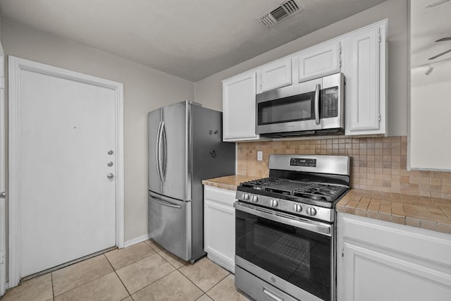kitchen featuring stainless steel appliances, tile countertops, white cabinetry, and decorative backsplash