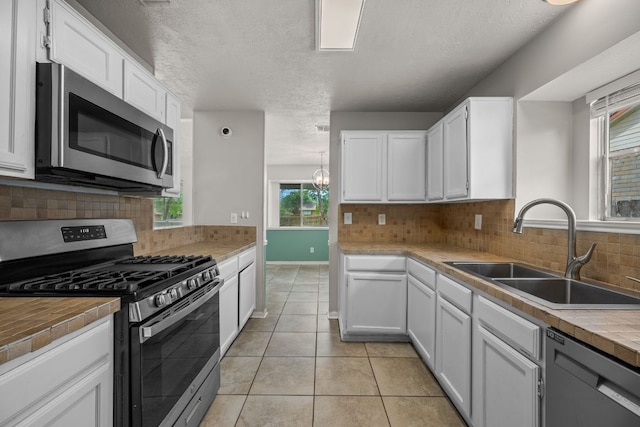 kitchen featuring appliances with stainless steel finishes, a sink, white cabinets, light tile patterned flooring, and decorative backsplash