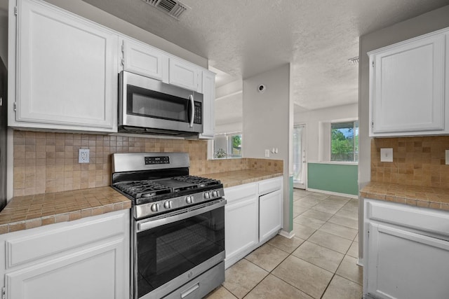 1605 Quail Run Rd, Pflugerville, TX 78660 - kitchen featuring appliances with stainless steel finishes, white cabinetry, light tile patterned floors, backsplash, and tile countertops