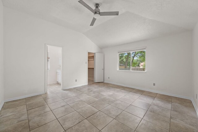 unfurnished bedroom with lofted ceiling, light tile patterned floors, a spacious closet, baseboards, and a closet