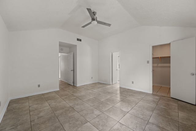 unfurnished bedroom with lofted ceiling, light tile patterned flooring, a ceiling fan, a walk in closet, and a closet