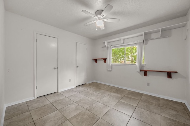 unfurnished bedroom with a textured ceiling, light tile patterned floors, baseboards, and ceiling fan