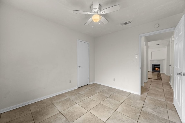 unfurnished bedroom featuring light tile patterned floors, a lit fireplace, baseboards, and a ceiling fan