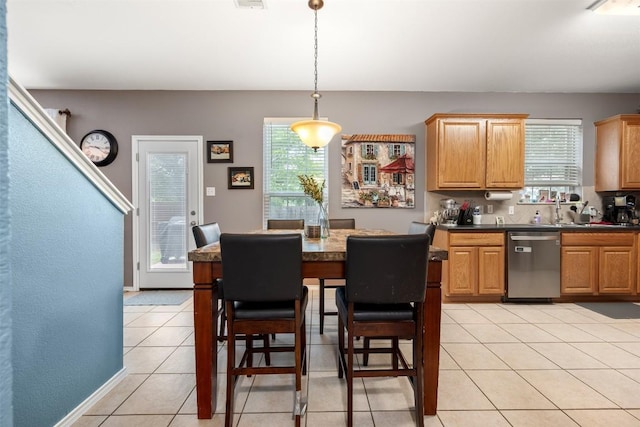 kitchen featuring dishwasher, dark countertops, light tile patterned floors, and hanging light fixtures