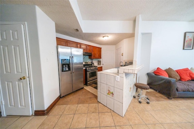 kitchen featuring stainless steel appliances, a textured ceiling, under cabinet range hood, tile counters, and light tile patterned flooring
