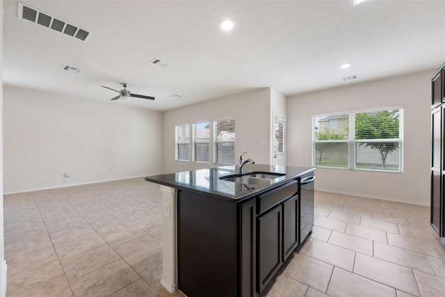 kitchen with a sink, dishwasher, light tile patterned floors, dark stone counters, and ceiling fan