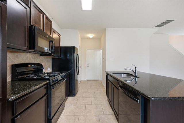 kitchen featuring black appliances, decorative backsplash, a kitchen island with sink, dark stone counters, and dark brown cabinetry