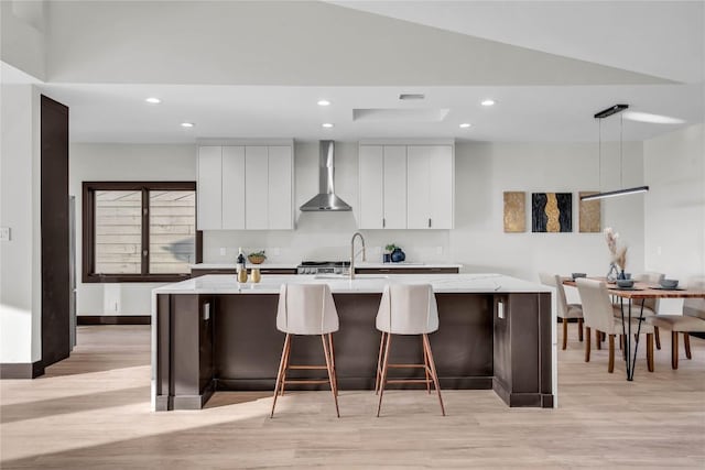 112 Paragon Ct, Lakeway, TX 78734 - kitchen with wall chimney range hood, light wood finished floors, recessed lighting, white cabinets, and a sink