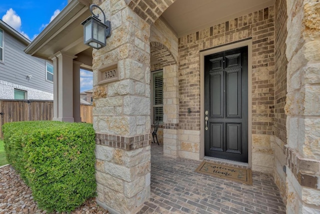 view of exterior entry with stone siding, fence, and brick siding