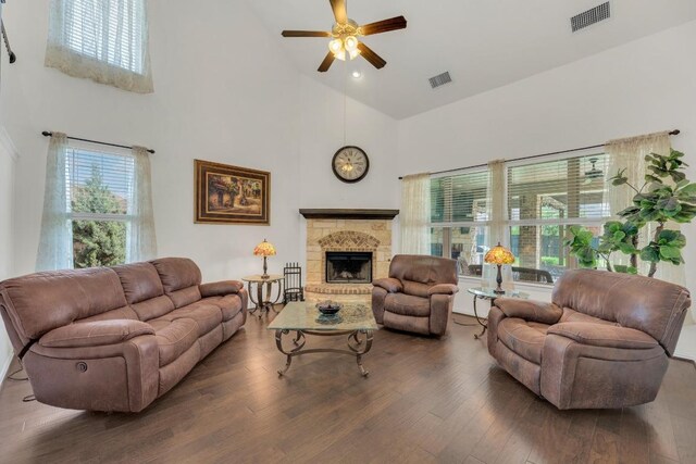 living area with high vaulted ceiling, a ceiling fan, wood finished floors, and a fireplace with raised hearth
