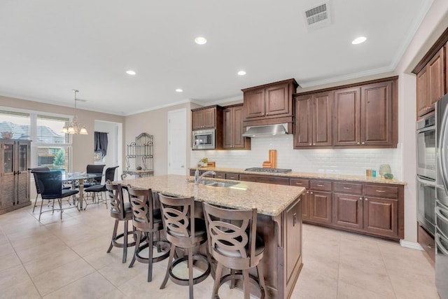 kitchen with appliances with stainless steel finishes, a sink, wall chimney range hood, light stone counters, and decorative backsplash