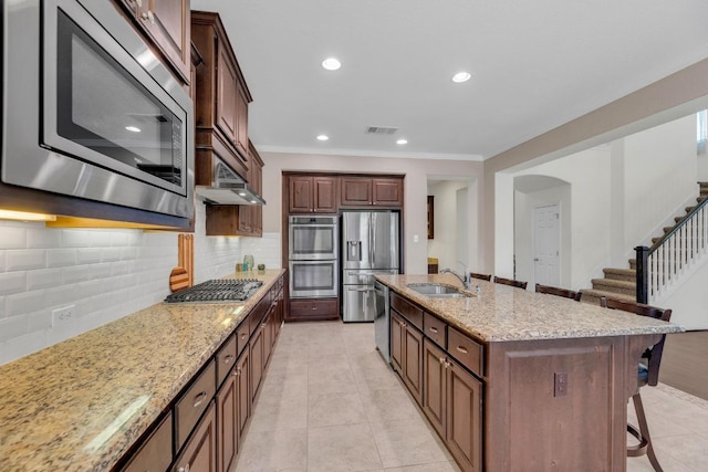 kitchen featuring stainless steel appliances, a sink, a kitchen bar, ornamental molding, and light stone countertops