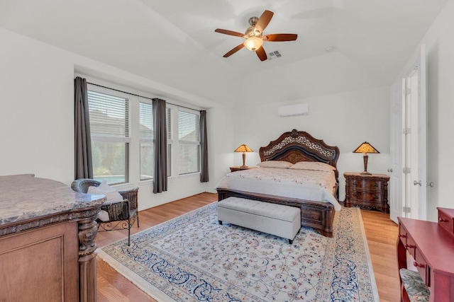 bedroom with ceiling fan, light wood-type flooring, a tray ceiling, and a wall unit AC