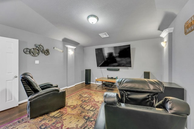 cinema room featuring wood finished floors, decorative columns, baseboards, and vaulted ceiling