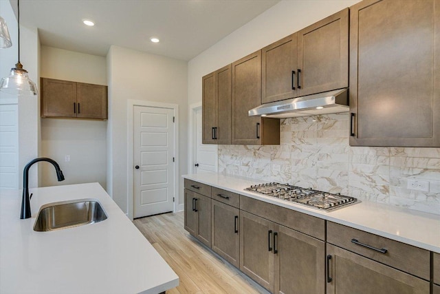 1401 S Brook Dr, Leander, TX 78641 - kitchen featuring under cabinet range hood, stainless steel gas stovetop, light countertops, backsplash, and light wood finished floors