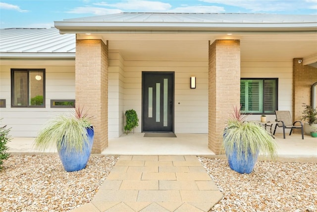 entrance to property with a standing seam roof, brick siding, covered porch, and metal roof