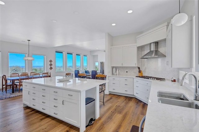 kitchen with wall chimney range hood, a sink, tasteful backsplash, light wood-type flooring, and white cabinetry