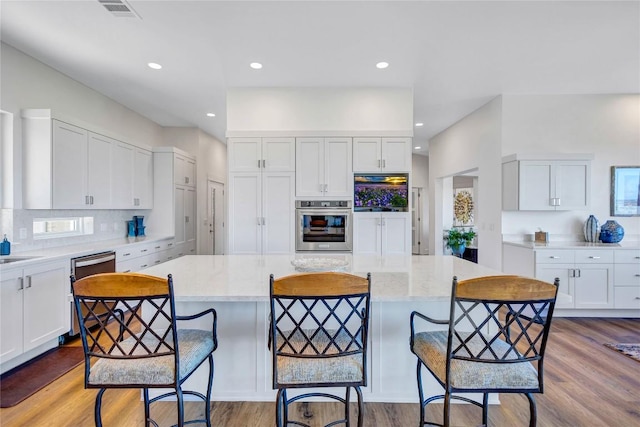 kitchen featuring oven, white cabinets, wood finished floors, dishwashing machine, and a kitchen bar