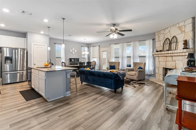 living area with light wood-style flooring, ceiling fan, recessed lighting, and a stone fireplace