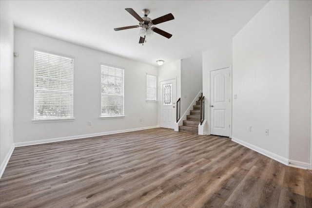 unfurnished living room featuring ceiling fan, stairs, wood finished floors, and baseboards