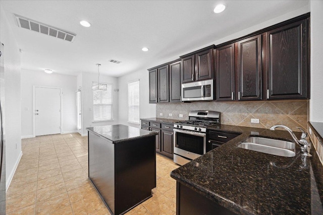 kitchen featuring appliances with stainless steel finishes, a sink, a center island, dark stone countertops, and tasteful backsplash