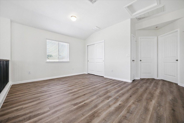 unfurnished bedroom featuring wood finished floors, lofted ceiling, attic access, baseboards, and a closet