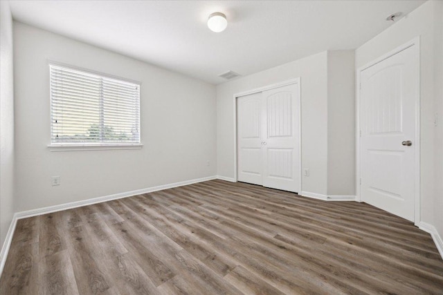 unfurnished bedroom featuring wood finished floors, a closet, and baseboards