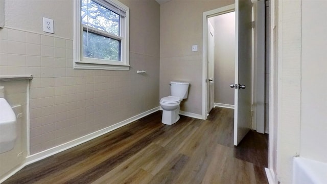 bathroom with tile walls, wood finished floors, toilet, and baseboards