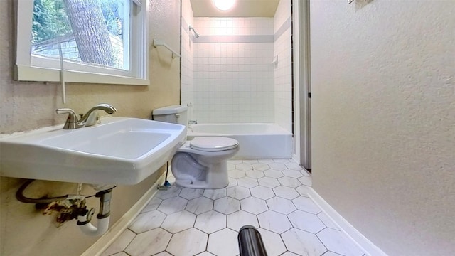 full bathroom featuring toilet, tile patterned floors, a textured wall, baseboards, and bathtub / shower combination