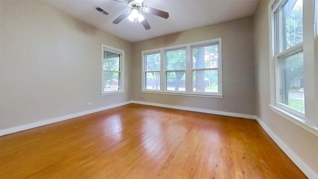 unfurnished room featuring healthy amount of natural light, baseboards, wood finished floors, and a ceiling fan