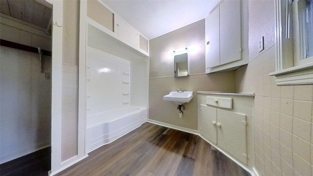bathroom with tile walls, wood finished floors, a tub, a sink, and baseboards