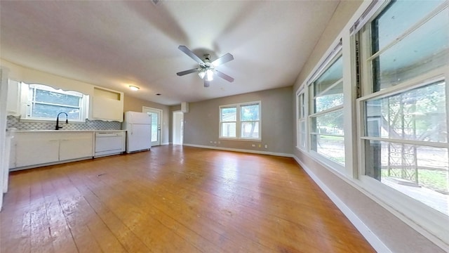 unfurnished living room with baseboards, light wood-type flooring, a ceiling fan, and a sink
