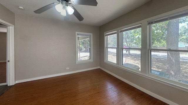 empty room featuring baseboards, plenty of natural light, dark wood-type flooring, and a ceiling fan