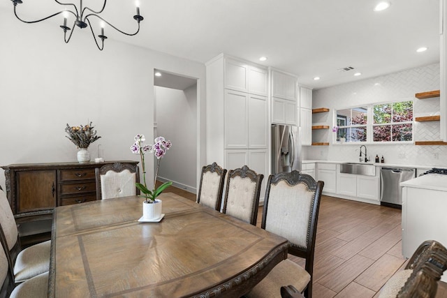 dining room featuring a chandelier, light wood-style flooring, recessed lighting, and bar with sink