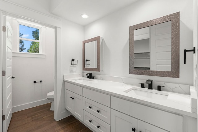 bathroom with wood finished floors, toilet, double vanity, baseboards, and recessed lighting