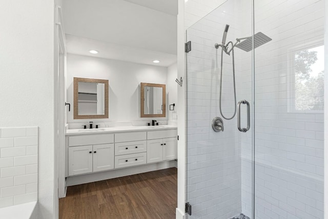 bathroom featuring a stall shower, wood finished floors, double vanity, and recessed lighting