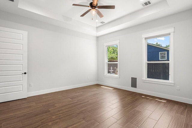 empty room with a tray ceiling, dark wood-type flooring, ceiling fan, and baseboards