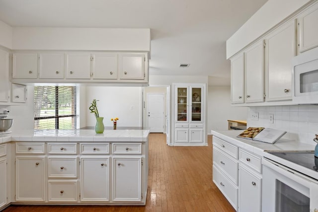315 Juniper Dr, Mountain City, TX 78610 - kitchen with white appliances, white cabinetry, a peninsula, light wood-style floors, and backsplash