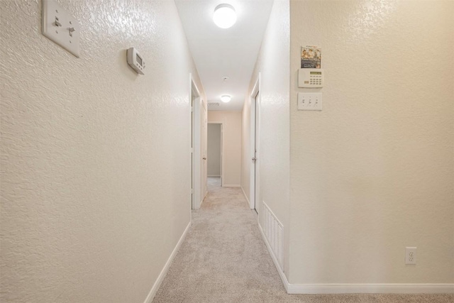 corridor with light carpet, a textured wall, and baseboards